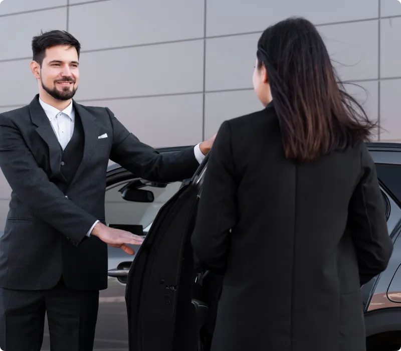 A uniformed chauffeur is welcoming a client and having a meet and greet session with them