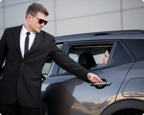 A chauffeur is about to open a car door to help a client