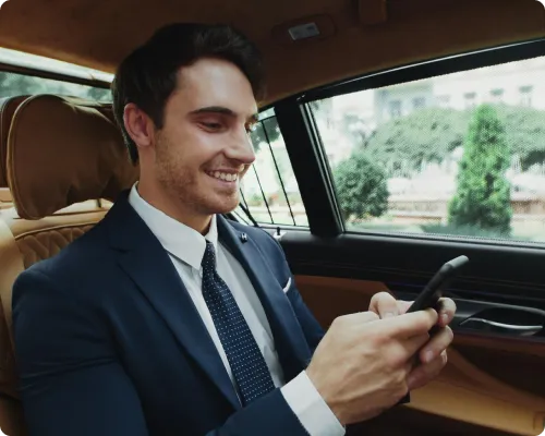 A business executive is smiling at his phone's screen while traveling in a limo