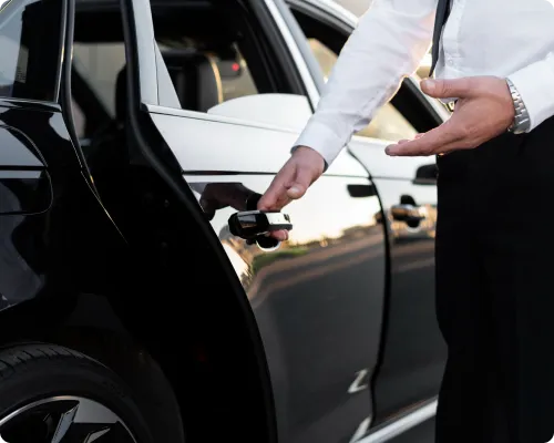 A chauffeur is opening the limo door for his clients and will drop them off at a concert in Milford