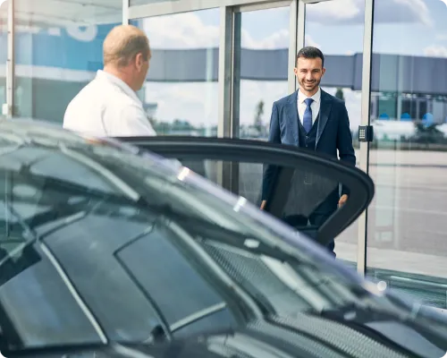 A uniformed chauffeur is seeing off a client after their trip from JFK to Manhattan