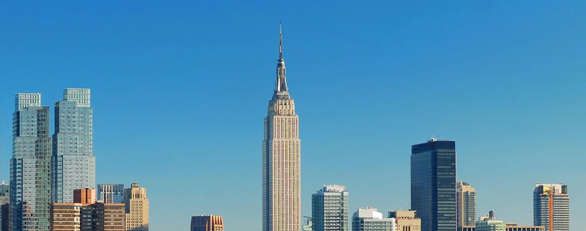 The image features a view of the Manhattan skyline with the Empire State Building prominently visible against a clear blue sky.