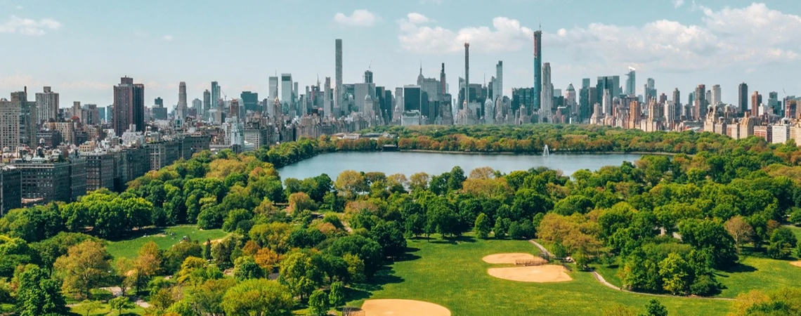 An aerial view of Central Park in Manhattan with a lush green landscape and the city skyline in the background.