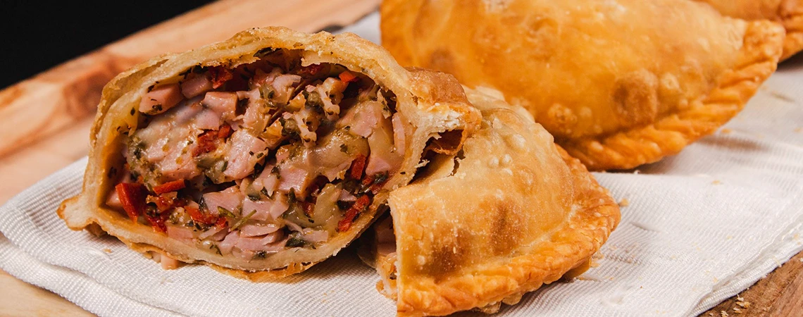 The image features a close-up of empanadas on a wooden board with one cut open to show the filling.