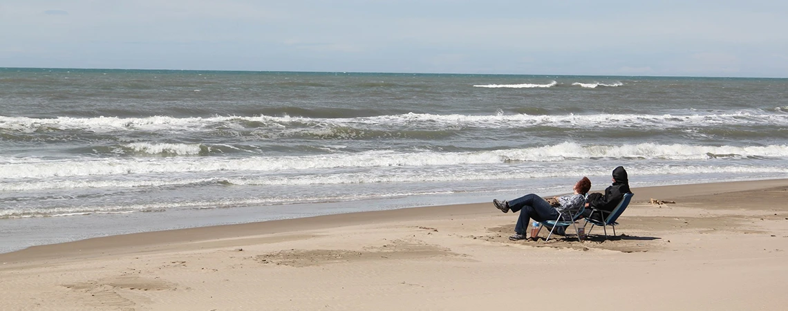 Two people relax in chairs on a quiet beach with waves in the background, illustrating scenic attractions like Jones Beach and Idlewild Park along the JFK to Long Island route.