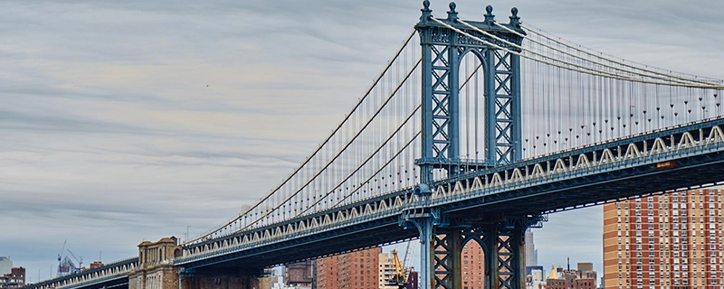 A picturesque view of the Brooklyn Bridge stretching over water with a city skyline in the background, leading to Brooklyn Bridge Park. The scene showcases a family-friendly destination with stunning views, promoting a safe and comfortable journey for kids with child safety seat options.
