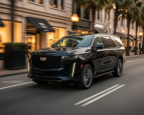 Hoboken Car Service's sleek black Cadillac Escalade SUV gliding along an elegant evening street lined with upscale boutiques, glowing storefront awnings, palm trees, and vintage lamps, offering premium chauffeured rides for Hoboken's vibrant nightlife and city explorations.