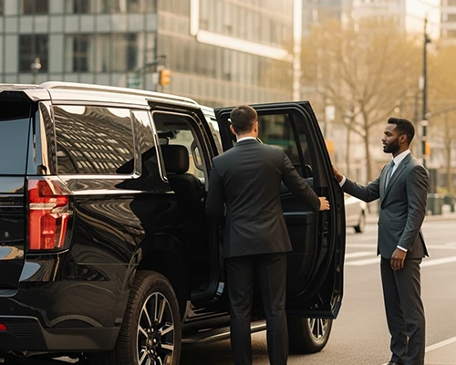 A professional chauffeur under JFK Airport transfer opens the door of a luxury black SUV for a business traveler on a city street, providing premium JFK airport transfer service.