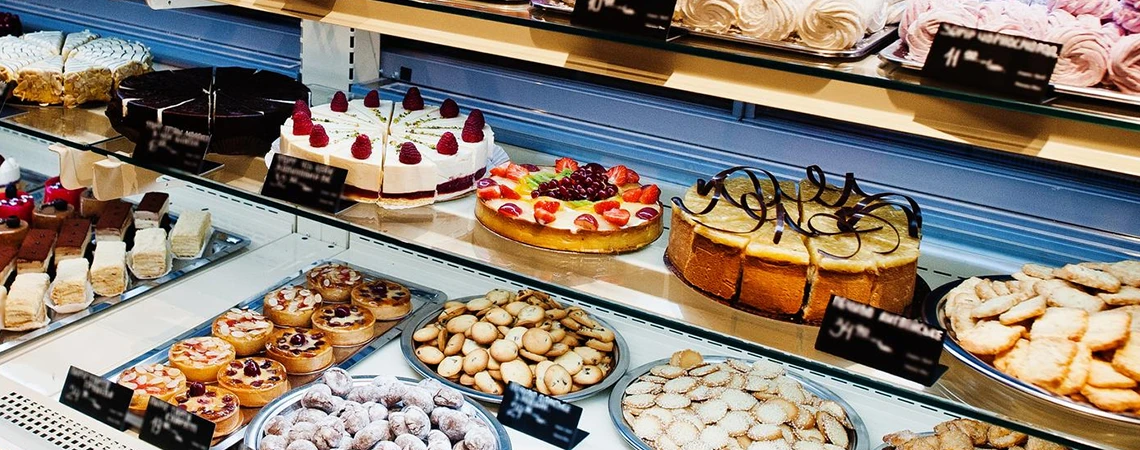 Hoboken Car Service to Quick Bite Spots: Vibrant bakery display case overflowing with decadent cakes topped with fresh berries, chocolate tarts, flaky pastries, and cookies, promoting sweet treats at Carlo's Bakery.