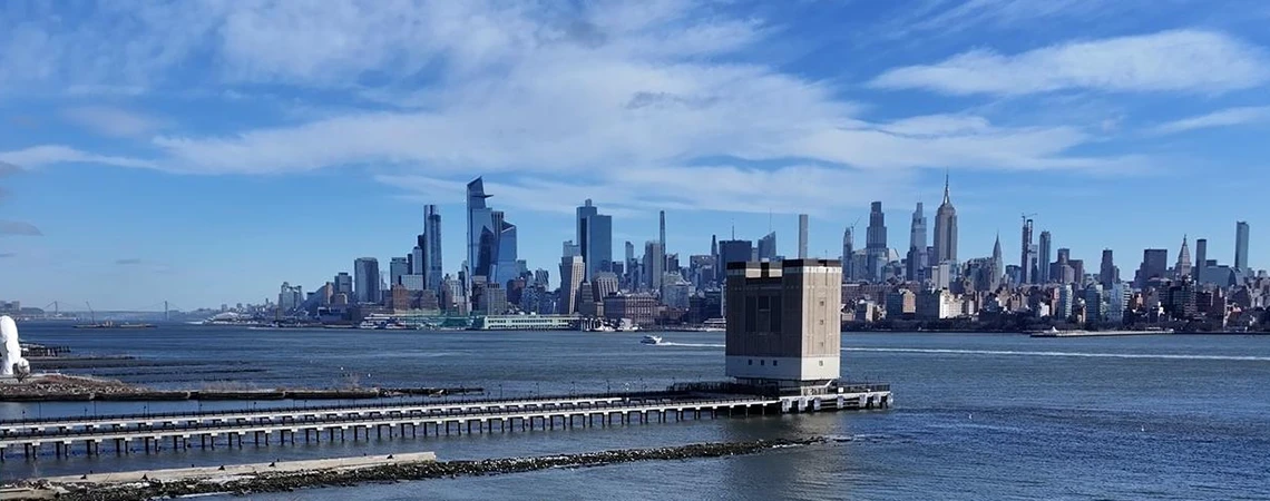 Hoboken Car Service for a Perfect Day Out: A scenic panorama of the Hoboken Waterfront, featuring stunning Hudson River views of the NYC skyline and lush green spaces under blue skies—ideal for chauffeured tours with friends and family to explore waterfront sights, outdoor fun, and vibrant Washington Street nightlife bars.