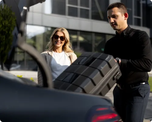 A chauffeur is helping a client with her luggage by loading the luggage in the car