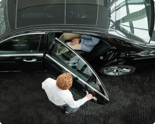 A bird eye view of a chauffeur holding a luxury car's door open for a client