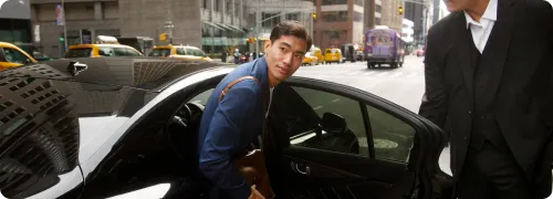 An asian business executive in blue suit is getting off the vehicle at Kings Point with the help of NYC United limo’s chauffeur.