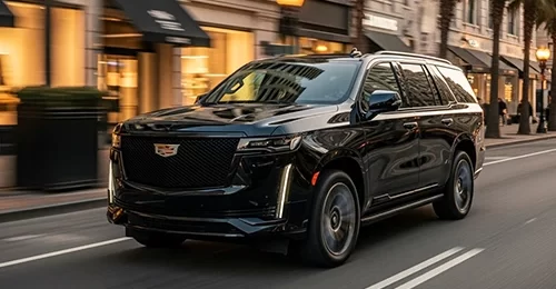 Hoboken Car Service's sleek black Cadillac Escalade SUV gliding along an elegant evening street lined with upscale boutiques, glowing storefront awnings, palm trees, and vintage lamps, offering premium chauffeured rides for Hoboken's vibrant nightlife and city explorations.